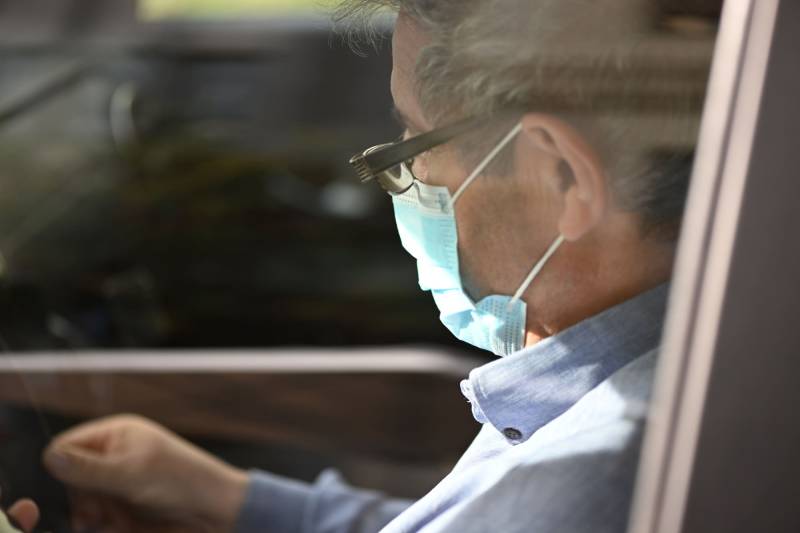 Chauffeur portant un masque médical dans une voiture, assurant un transport sécurisé pour les patients