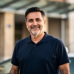 Homme souriant en polo devant un bâtiment